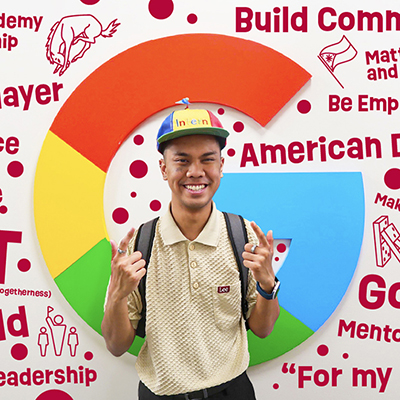 Matt Mayo wears Google "intern" beanie with propeller, standing in front of wall with "G" Google logo 