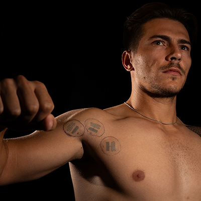 Nick Cmager stands shirtless with three microfluidic sensors stuck to his skin above his armpit.