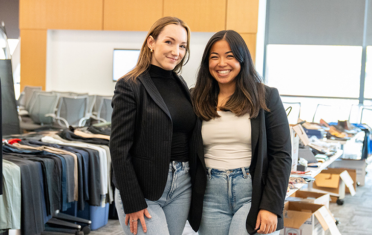 Victoire Marion (left) and Kalena Paredes stand in front of tables of donated professional clothing