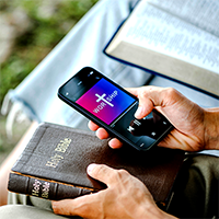 Hands holding a bible and a smartphone displaying a biblical app